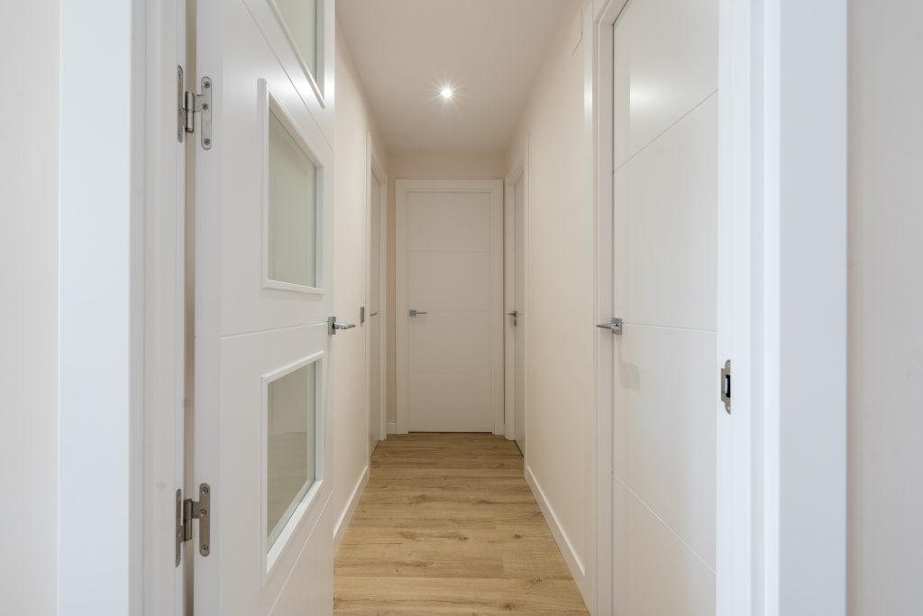 Pasillo de vivienda con suelo laminado y puertas blancas.